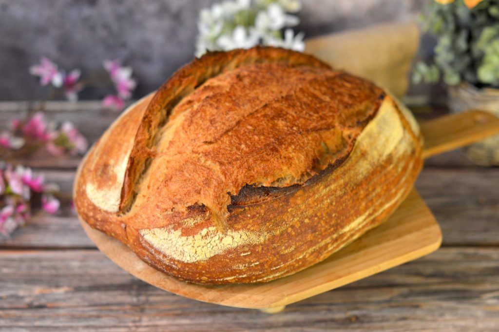 Hogaza de pan casero con masa madre, corteza dorada y greñado abierto sobre una tabla de madera